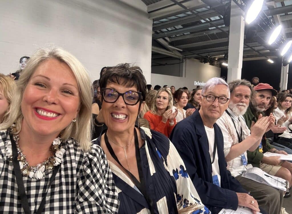A group of people sitting in rows at an indoor event, some smiling and some clapping.