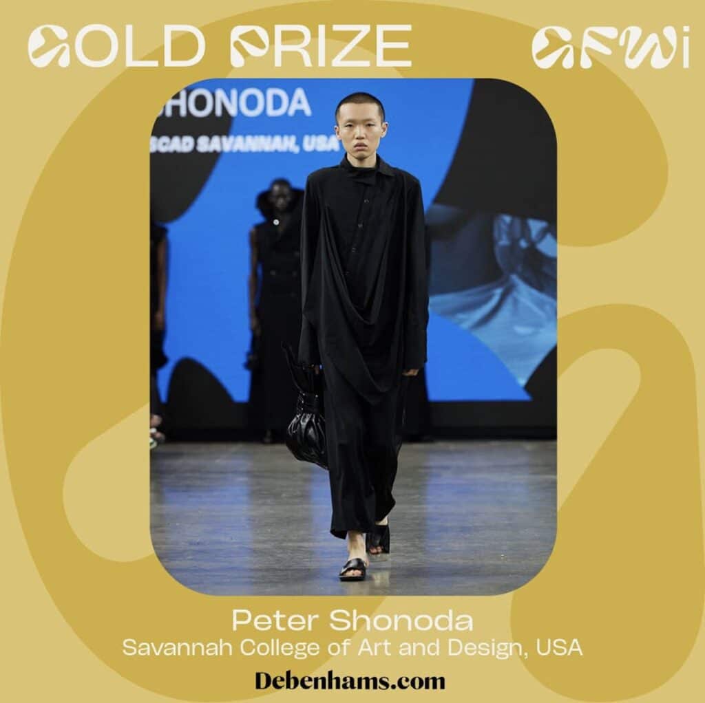 Person wearing a long black outfit walks on a runway. Text reads "Gold Prize" and "Peter Shonoda, Savannah College of Art and Design, USA." Fashion event backdrop and branding visible.
