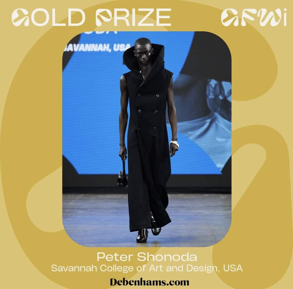 Model in a long, sleeveless black coat walks the runway. The backdrop reads "Gold Prize AFWI" with "Peter Shonoda, Savannah College of Art and Design, USA" below.
