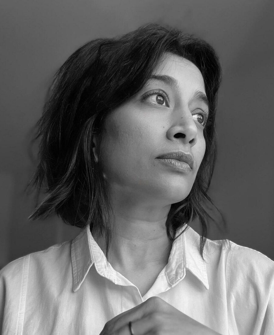 A woman with short hair looks to the side in a black and white photo, wearing a white button-up shirt.